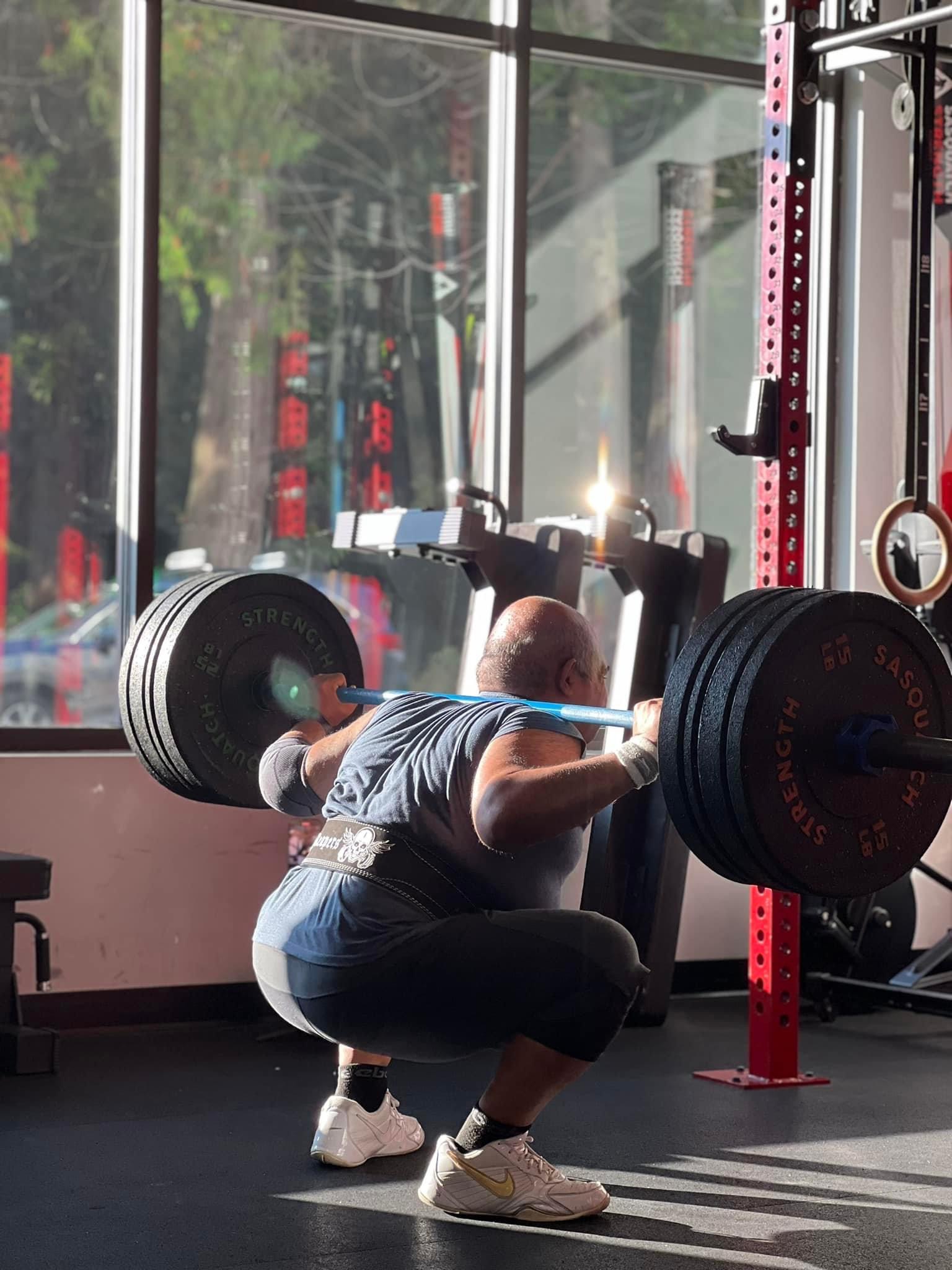 Member squatting at a red power rack during a coached strength session at Sasquatch Strength