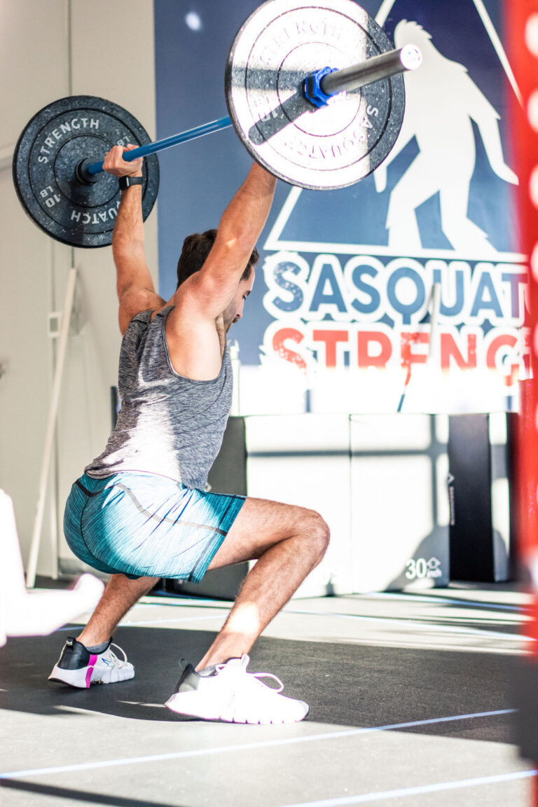 Member lifting a barbell overhead during strength training at Sasquatch Strength near Sammamish